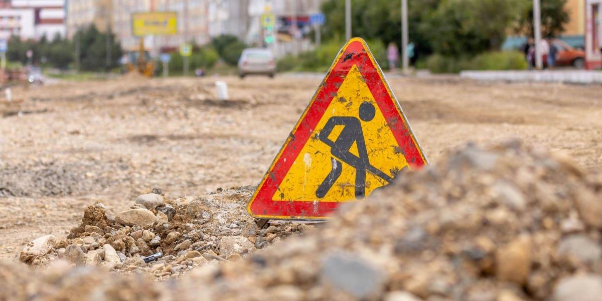 Yellow triangle warning sign indicating road work on an urban street under construction.